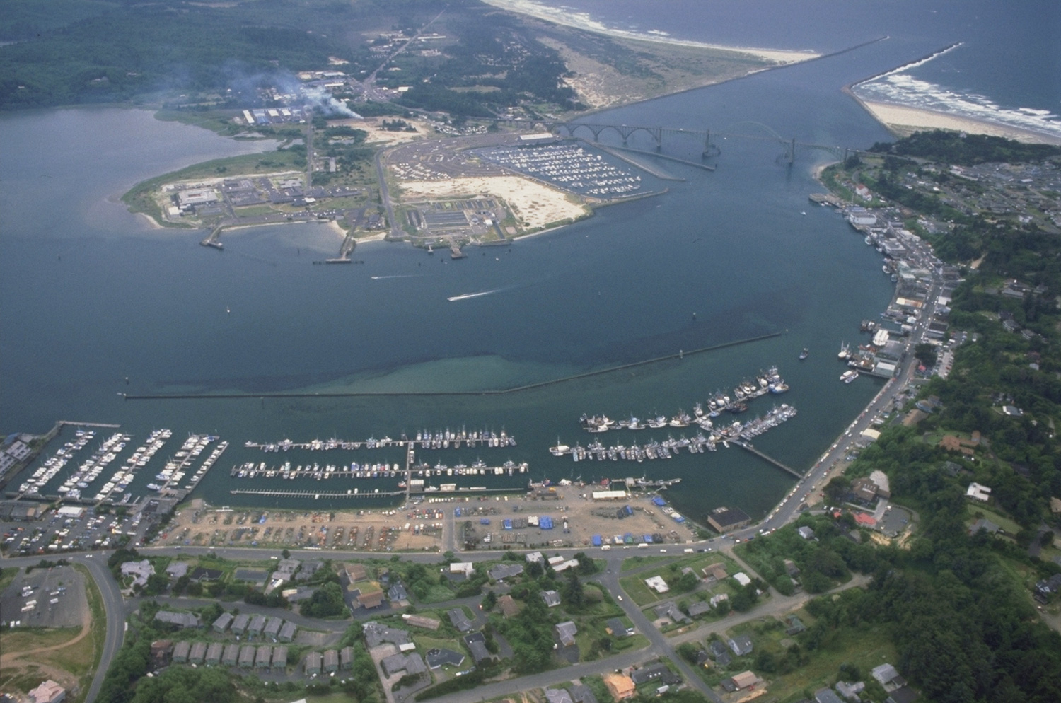 Aerial view of Yaquina Bay in Newport, Oregon — the marina, fishing fleet, Yaquina Bay Bridge, and the road along the bay
